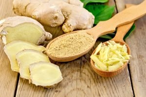 Grated and ground ginger in two wooden spoons ginger root green leaves on the wooden board